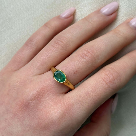 Gold ring with a green gemstone on a hand with light pink nail polish.