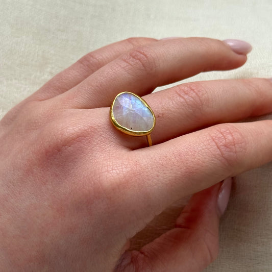 Hand wearing a 22ct gold ring with a large, faceted Moonstone gemstone on a neutral background