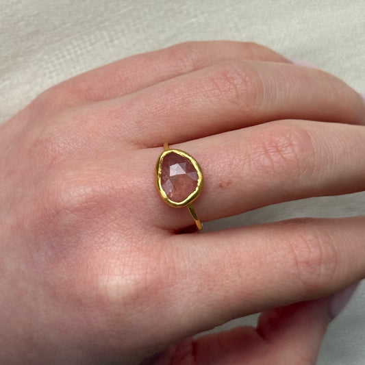 22ct Gold ring with a pink sapphire on a person's finger against a neutral background