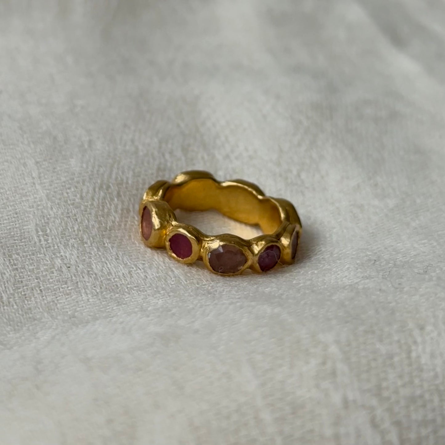 22ct Gold ring with embedded pink tourmaline stones on a light gray fabric background