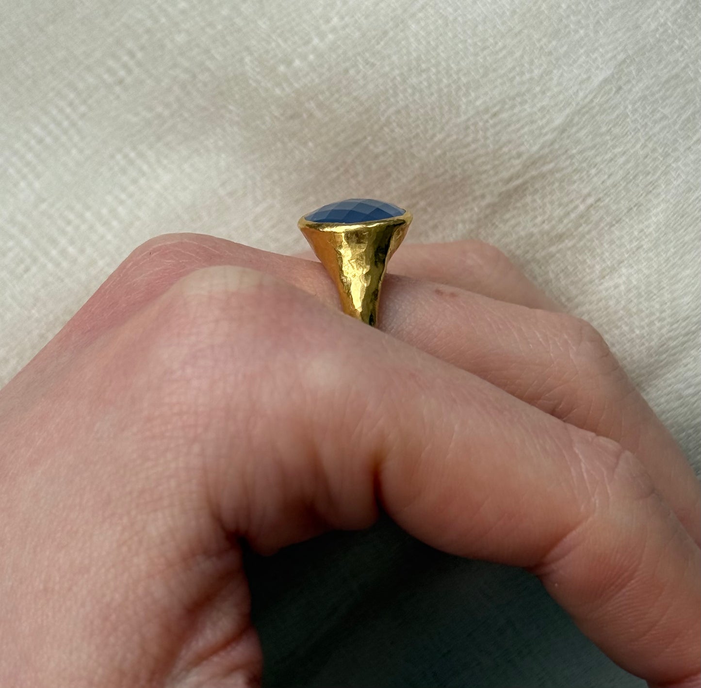 22ct Gold ring with a blue stone on a finger against a white background