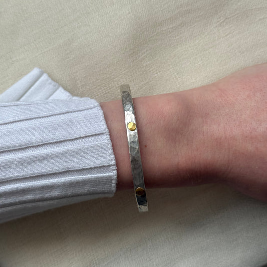 Silver bracelet with 22ct gold accents on a wrist against a beige background