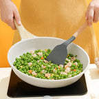 Person cooking peas and shrimp in a white bowl with a spatula on a yellow background