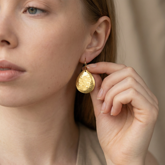 Close-up of a woman wearing gold teardrop earrings, holding one with her hand.
