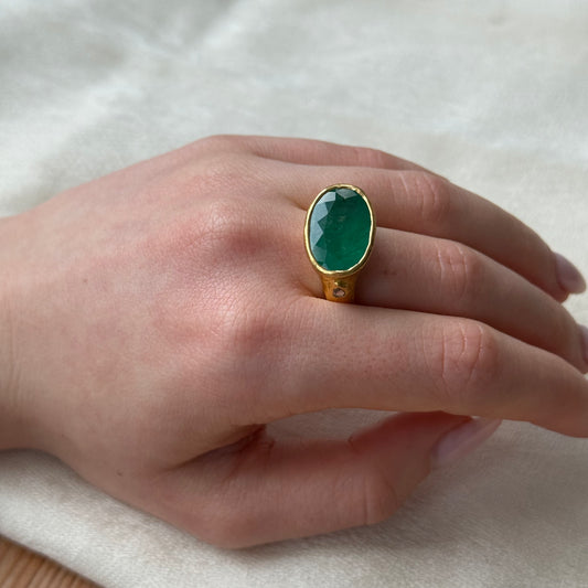 Hand wearing a 22ct gold ring with a Emerald  gemstone on a light background