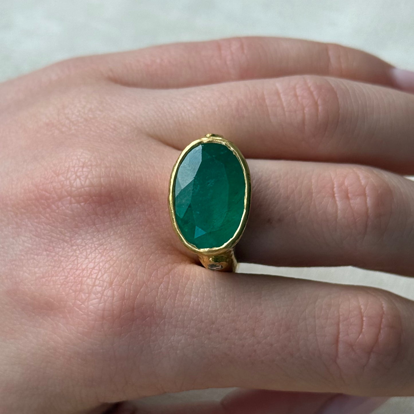 Emerald gemstone ring with 22ct gold setting on a hand against a neutral background