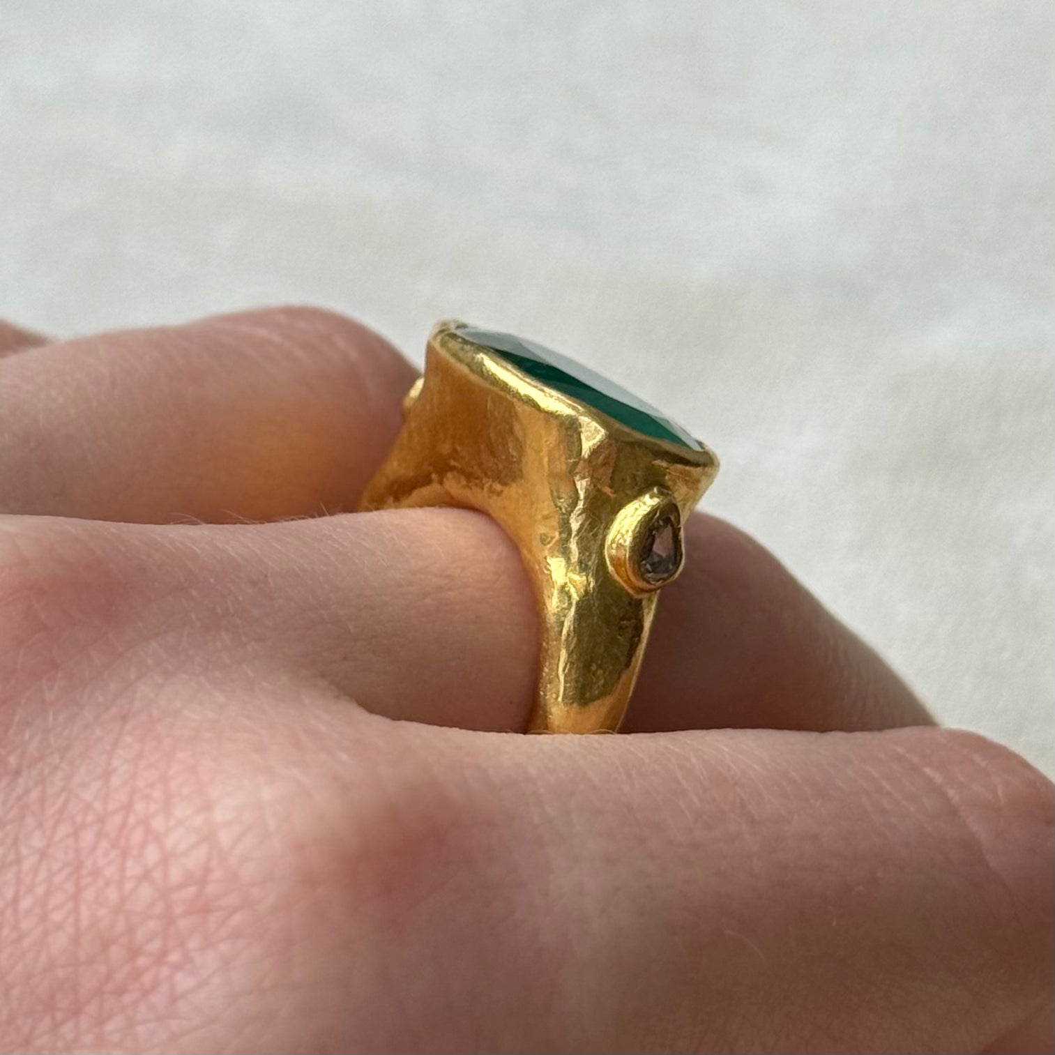 22ct Gold ring with a Emerald gemstone on a finger against a white background