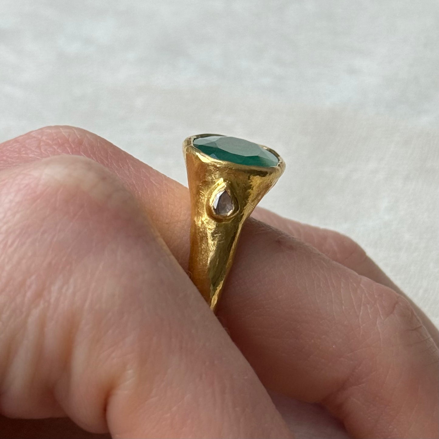 22ct Gold ring with a Emerald gemstone on a finger against a white background