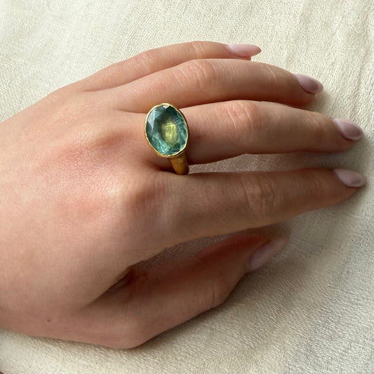 Hand wearing a ring with a blue aquamarine gemstone on a light background