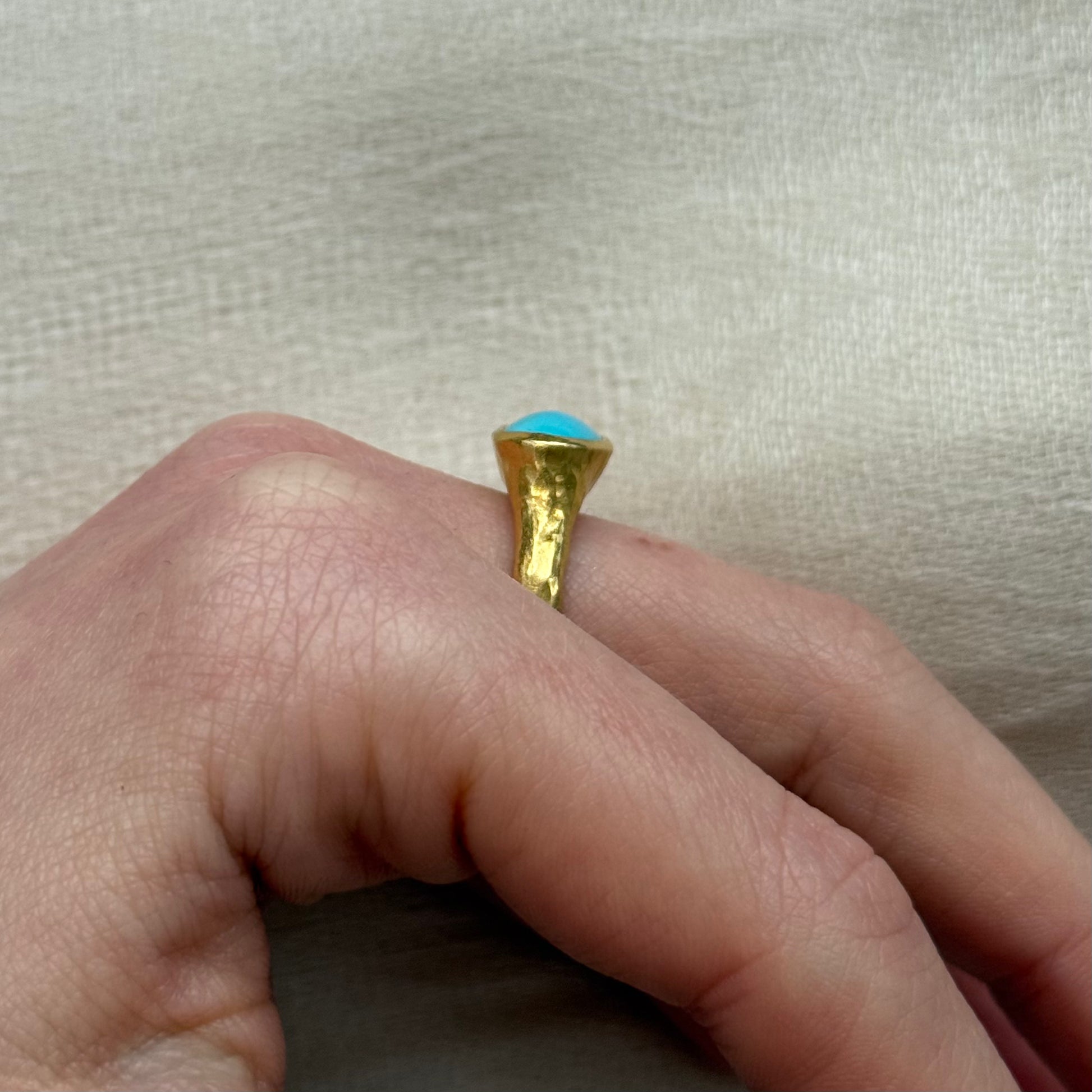 22ctGold ring with a blue gemstone on a finger against a beige fabric background