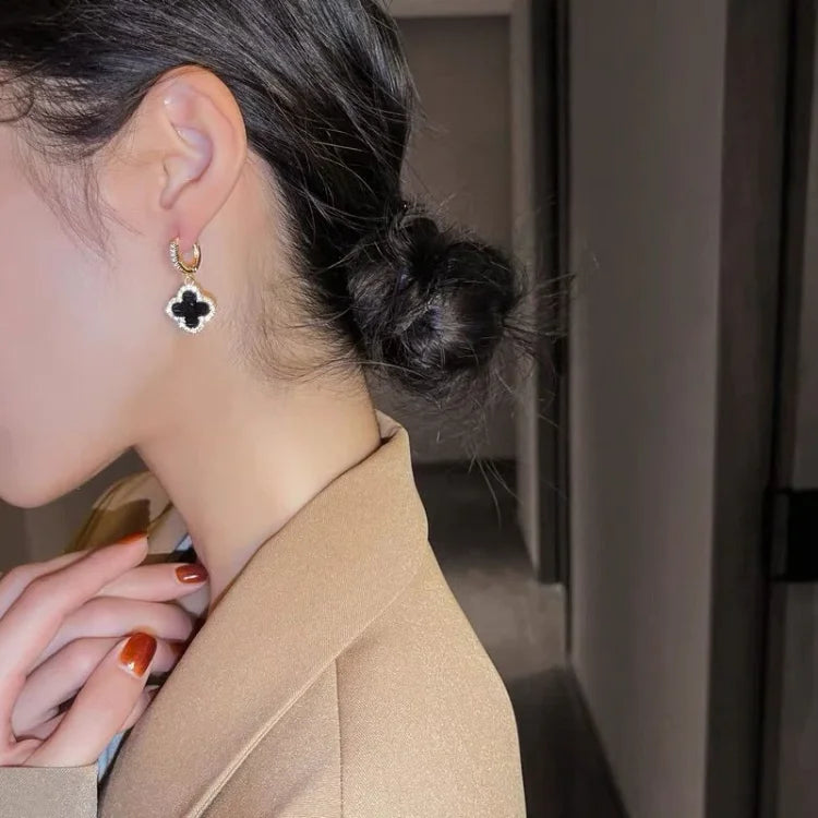 Close-up of a person wearing a clover-shaped earring with a neutral background