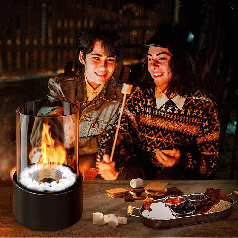 Two people roasting marshmallows over a portable fire pit with s'mores ingredients on a wooden table.