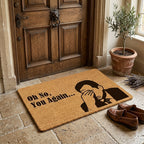 Doormat with humorous design and text in front of a wooden door.