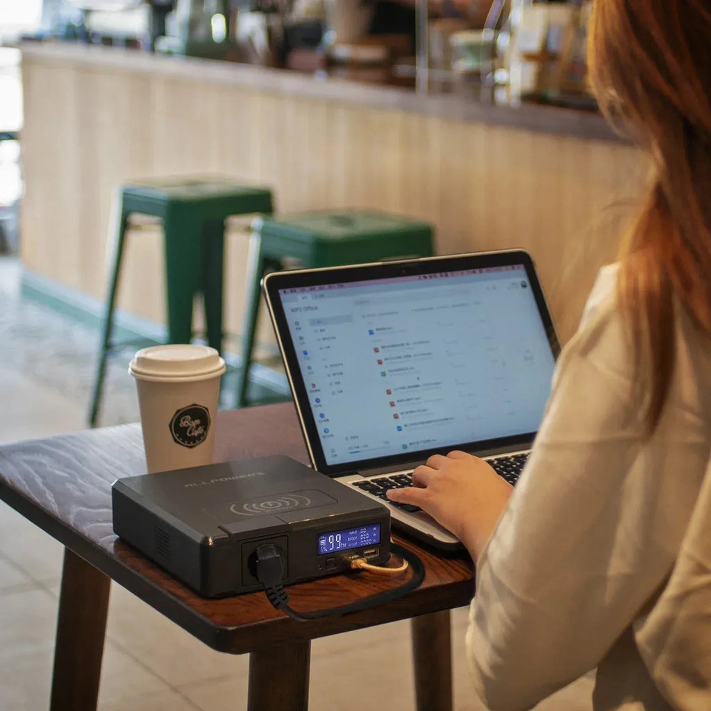Person using a laptop with a portable power station on a table in a cafe.