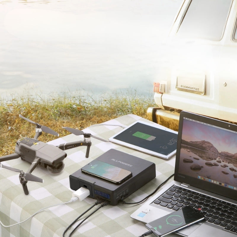 Tech devices including a drone, laptop, tablet, and smartphone on a table with a scenic background.
