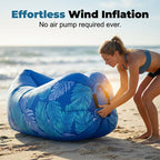 Woman inflating a blue inflatable lounge on a beach with text about effortless wind inflation.