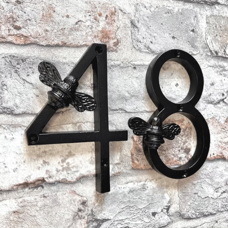 Black house numbers '48' with bee designs on a stone wall.