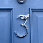 Silver door knocker shaped like the number '3' with a bee design on a blue door.
