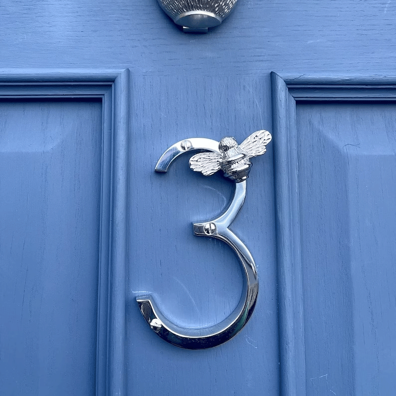 Silver door knocker shaped like the number '3' with a bee design on a blue door.