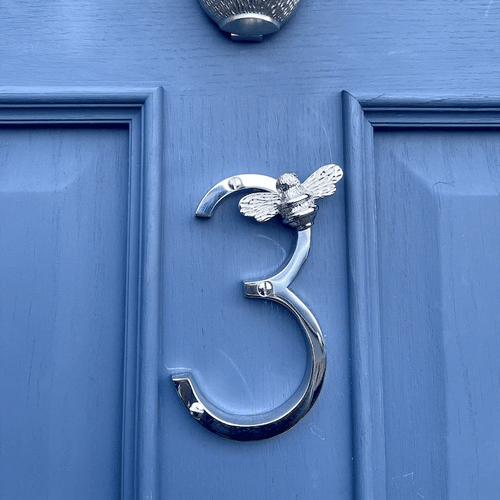 Silver door knocker shaped like the number '3' with a bee design on a blue door.