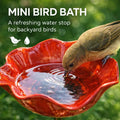Red mini bird bath with a bird drinking water, set against a green background.