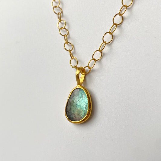 Pendant with a 22ct gold pendant featuring a Labradorite gemstone on a light gray background. Designer is Ram Rijal.