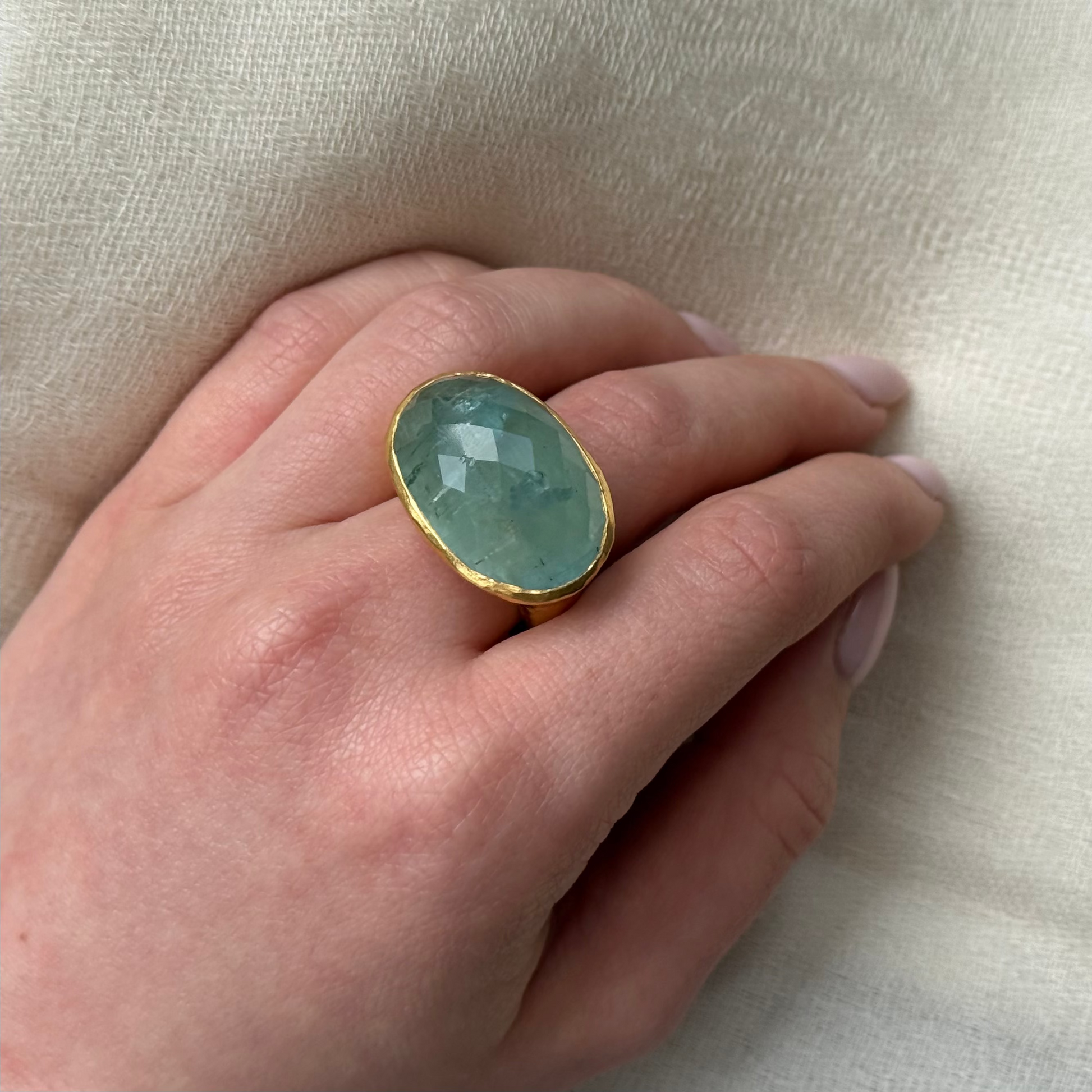 Hand wearing a ring with a Aquamarine gemstone on a beige background