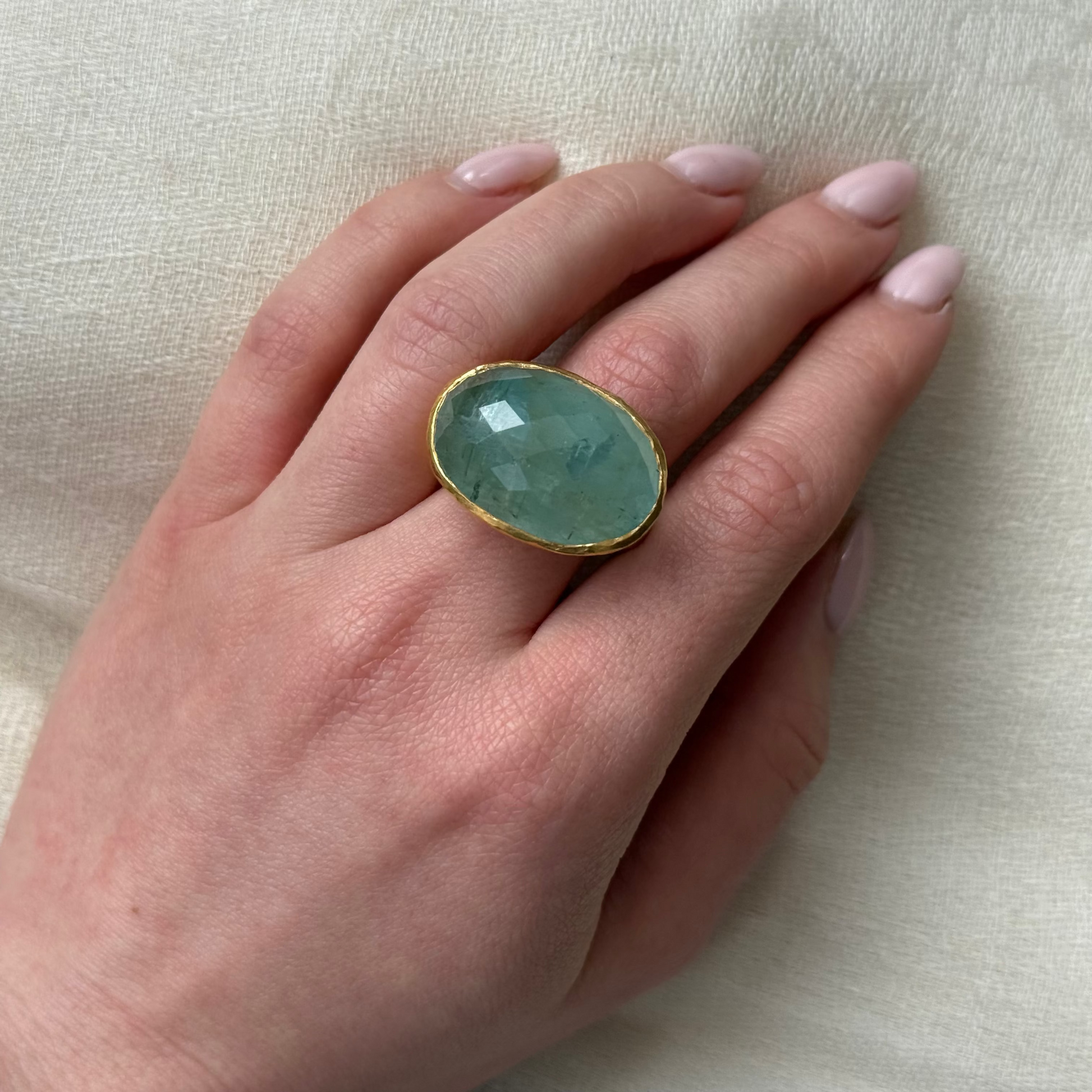 Hand wearing a ring with a 22ct Solid Gold Aquamarine gemstone on a beige background