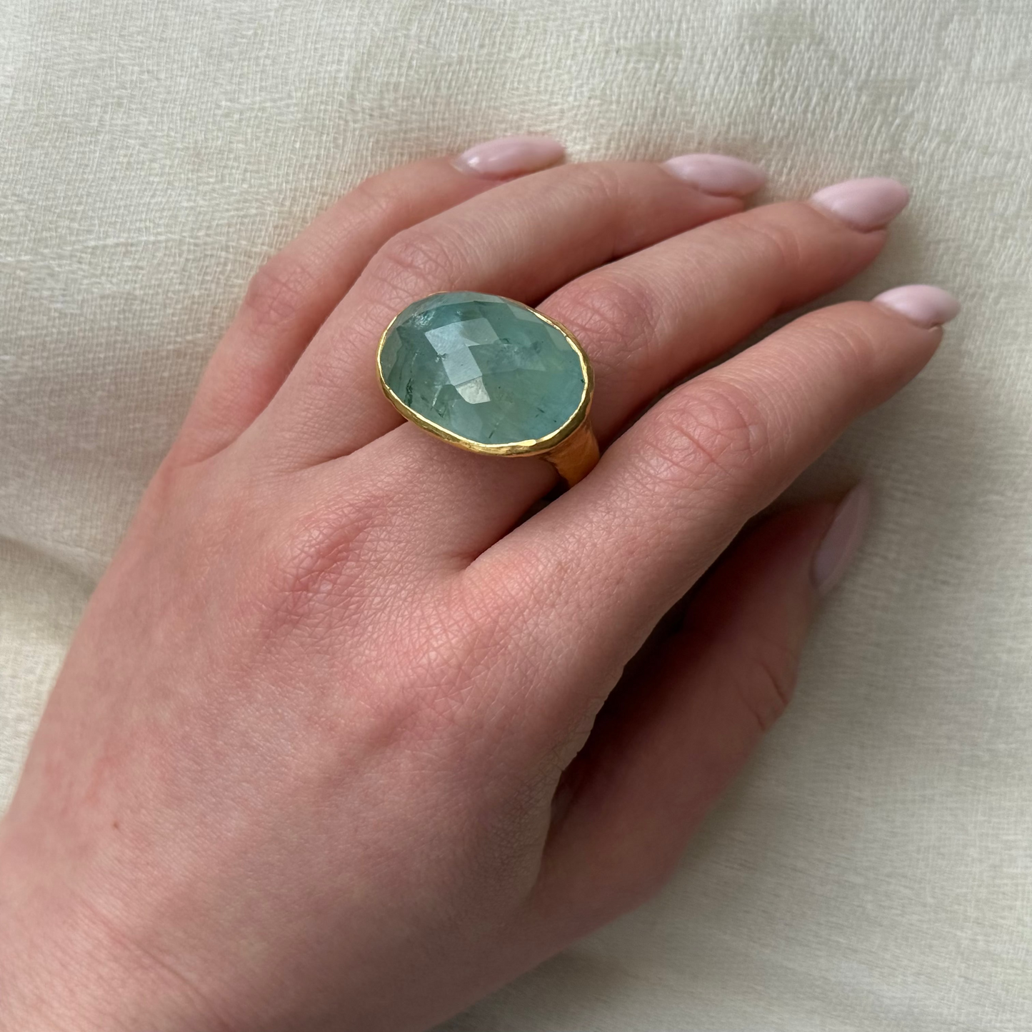 Hand wearing a ring with a Aquamarine gemstone on a light background