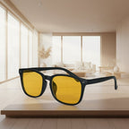 Sunglasses with yellow lenses and black frame on a wooden surface in a bright room.