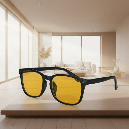 Sunglasses with yellow lenses and black frame on a wooden surface in a bright room.