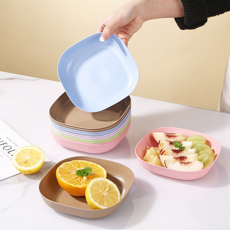 Colorful stack of square plates with a hand lifting one, on a light surface with fruit and a lemon.