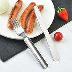 Stainless steel fork and knife set on a plate with sausages and vegetables.