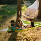 People sitting in green hammocks in a grassy outdoor area with a tent in the background.