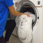 Person placing a fluffy white pillow into a washing machine with text 'Fully Machine Washable'.