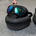 Black goggles with blue reflective lenses in a mesh carrying case on a gray surface.