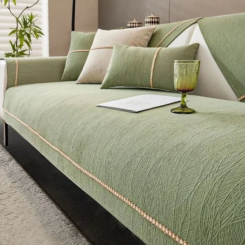 Green sofa with decorative pillows and a glass on a light-colored floor.