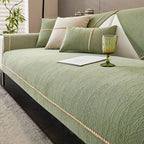Green sofa with decorative pillows and a glass on a light-colored floor.