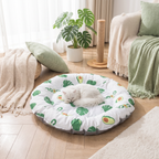 White cat sleeping on a round pet bed with green leaf pattern in a cozy living room.