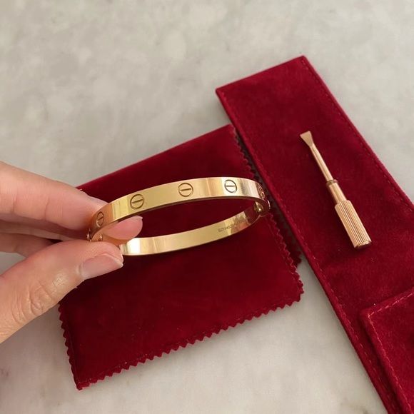 Gold bracelet held by a hand on a red velvet surface