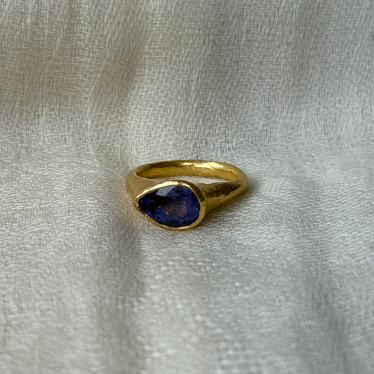 22ct Gold ring with a blue gemstone on a textured beige background
