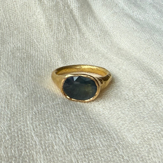22ct Gold ring with a dark blue sapphire gemstone on a light fabric background