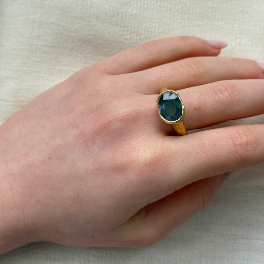 Hand wearing a 22ct gold ring with a blue sapphire on a neutral background