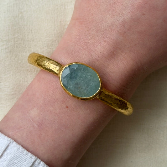 22ct Gold bracelet with a Aquamarine stone on a wrist against a beige background
