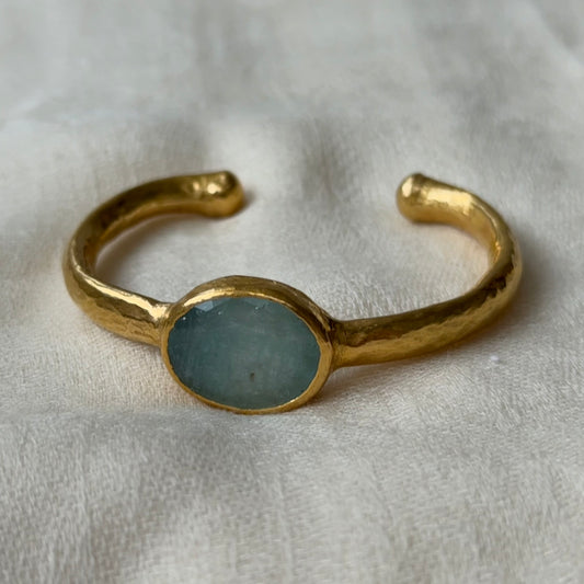22ct Gold bracelet with a central blue Aquamarine stone on a light fabric background