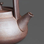 Close-up of a ceramic teapot with a dark brown handle on a gray background