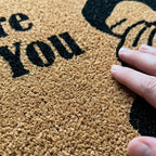 Doormat with text and a hand touching it