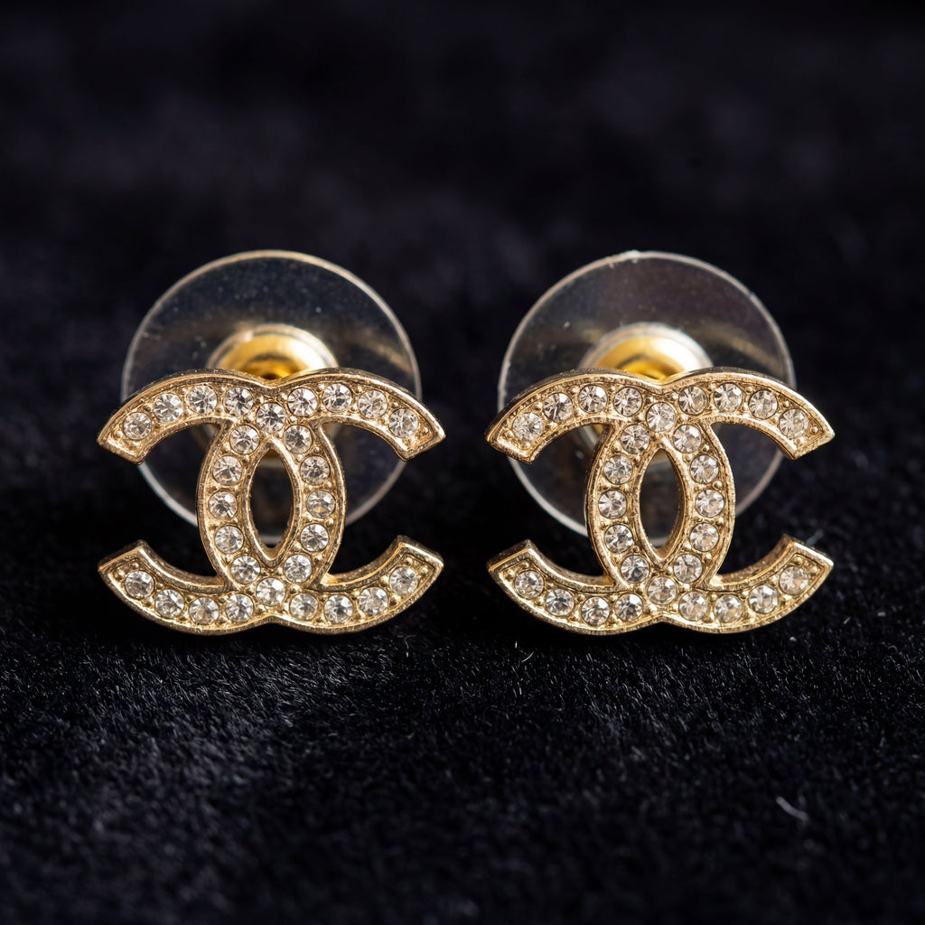 Gold Chanel earrings with clear gemstones on a black background