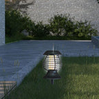 Solar-powered outdoor light fixture on grass with a stone wall and plants in the background