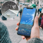 Person holding a smartphone with a weather app displaying outdoor temperature, rain sensor icon, and Wi-Fi signal.